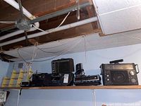 Wide shot of six radios and small yellow display shelf placed on a shelf against a light blue wall below an unfinished ceiling.