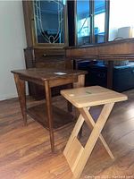 Photo showing two side tables: a larger wooden side table with lower shelf and a smaller collapsible wooden side table with crossed legs.