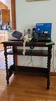 Front view of the side table with carved legs and magazine rack. Shows arrangement of phones and answering machine on top.