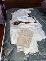 Photo of folded white and cream crocheted doilies, napkins, and tablecloths on a mattress.