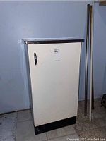 Full view of the cabinet with door closed showing cream-colored door, black base, and metal handle.