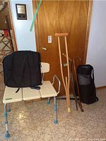 Photo showing the accessible shower bench, yoga mat in carrying bag, crutch, wooden canes, shoe horn, and athletic bags all grouped together in front of a wooden door.