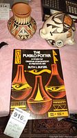 Photo showing one Acoma pottery vase, one white pottery piece with handles and geometric painted patterns, and The Pueblo Potter book.