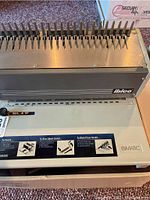 Close-up of the Ibimatic binding machine showing metal teeth comb opener and punched paper holder with Ibico branding