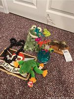 Photo showing brass lion statue on wooden base with frog plush animals, pirate sign, Hawaiian necklace and glass flower sculpture on the floor