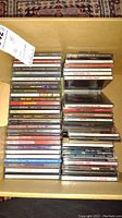 Photo of a full box containing about fifty CDs in jewel cases stacked in several columns, showing various album spines with artist names and album titles