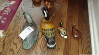 Photo showing three duck decoys placed on hardwood floor: large detailed painted duck, medium mallard style duck, and small rounded wooden doorstop duck