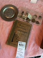 Photo shows metal dime tray, plastic case with foreign coins, and 'Alice's Adventures in Wonderland' book on pink fabric.
