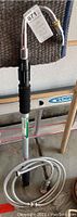 Full view of the Orbit telescoping wand with attached curved metal nozzle and black foam grip, resting beside a ladder and wooden broom handle.