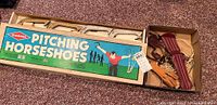 Pitching horseshoes game box with colorful family graphic, cardboard box with wooden game pieces inside