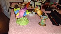 Photo of two ceramic bird figurines on a pink tablecloth, showing front and side views