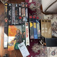 Top view of 20 classic movie VHS tapes arranged on carpet and floor. Titles include Braveheart, Star Wars, Jurassic Park, Hook, Robin Hood, Body Work, Bloodsport, Kill Switch, Men in Black.