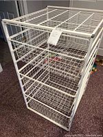 Front view of white metal wire storage rack showing 3 wire drawers with a label attached on top.