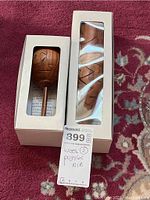 Two boxed wooden puzzles on a carpet, one rounded with handle, one slender