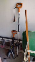 Full view showing jaw saw device and aluminum extender pole with orange handles, set against a wall with other tools nearby.