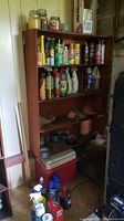 Wide shot of wooden shelf filled with various cleaning sprays, bug killers, duct tape rolls, and coolers beneath the shelf.
