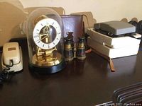 Photo showing vintage clock under glass dome with brass base, two pairs of optical devices (opera glasses and binoculars) on a dark surface.