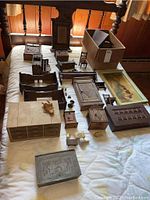 Bird's eye view of multiple miniature wooden dollhouse furniture pieces displayed on a bed including cabinets, tables, and small chests.