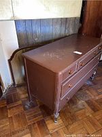Brown vintage wooden dresser with four drawers, facing left, showing chipped paint, one drawer knob missing