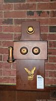 Front view of the vintage wooden telephone drink cabinet with eagle emblem and handset mounted on the side.