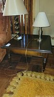 Full view of dark wood vintage end table with two metal lamps on top and a yellow rug underneath.
