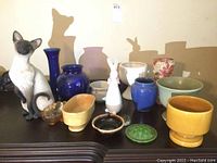 Overview of all figurines, vases and planters on a dark wood surface, including cat and bunny figurines and colorful vases.