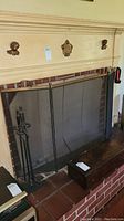 Wide shot showing the vintage fireplace screen in front of a fireplace with brick hearth and the fireplace tool stand with tools to the left.