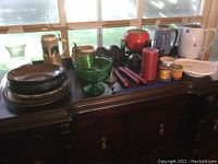 Photo displaying all items on dark antique sideboard with windows behind. Items include glassware, plates, bowls, footed candy dish, steins, candles, candle holders, and a red fondue pot.