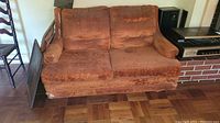 Front view of vintage brown love seat sofa with visible damage to upholstery and worn cushions.