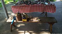 Photo showing one wooden bench with various tools and objects placed on it, viewed under an outdoor shaded area.