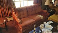 Vintage sofa with heavy upholstery damage on armrests and seat cushions. Fabric is torn with visible stuffing.