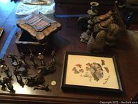 Photo showing metal toy soldiers, wood box, framed wall art, owl figurines, shoe figurines, elephant figurines, and candlestick holder on a table.