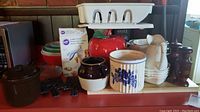 Overall lot showing multiple kitchen items including Corningware containers, wooden salt and pepper grinders, ceramic cookie jar, white dish strainer, and various bowls and pitchers