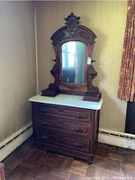 Front view of vintage wooden dresser with marble top and attached mirror in decorative carved wooden frame.