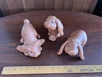 Three ceramic rabbit figurines shown from top-front angle on wooden surface, with measuring ruler for scale