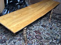 Full view of the wooden coffee table, showing the single wide board top and stick-constructed legs on a patterned rug.