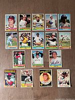 Top-down photo of 17 assorted vintage baseball cards arranged flat on wood floor, featuring various players like Rollie Fingers, Rudy May, and a 1959 George Anderson card.