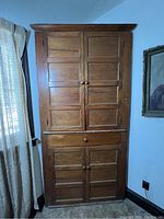 Front view of closed corner cabinet showing two upper and two lower raised panel doors, crown molding and plinth base.