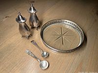 Sterling silver salt and pepper shakers, two small sterling salt spoons, and a Birks sterling bottle coaster on wooden surface.