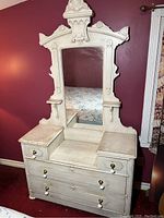 Front view of Victorian vanity showing white painted finish, large rectangular mirror, two surface drawers with brass knobs, and carved wooden crest detail.