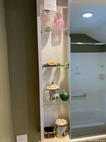 Shelf with assorted Asian themed decor - lidded cups, green figurines including frogs and turtles, glass perfume bottles on different shelves