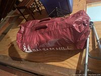 Red Balsam Hill branded storage bag fully closed, lying on a wooden floor
