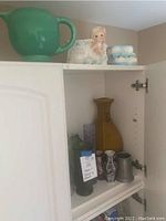 Shelf interior showing various decorative vases and containers, small glass bottle, metal and ceramic pieces, and a figurine
