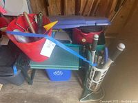 Side view of garden kneeling bench with blue recycling bin beneath, red bucket on top with hand tools, and green fabric tool holder attached with tools.