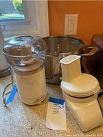 Sunbeam OSKAR food chopper and Emeril large stock pot with glass lid placed on a kitchen counter.