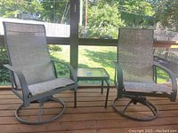 Photo showing two outdoor swivel chairs and a square glass top end table on a wooden deck with a screened porch background.