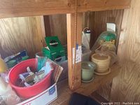 Shelf containing a variety of gardening-related items including pots, boxes of Miracle-Gro, spray bottles, and gardening tools inside a wooden shelf.