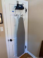 Photo of blue and black Rowenta Everlast iron placed on hanging rack mounted on door, with gray ironing board hanging below.