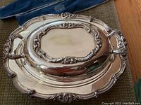 Ornate silver plate covered serving dish with floral and scroll edge detailing shown closed.