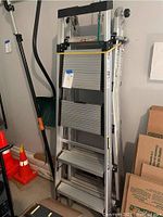 Front view of two aluminum multi-position ladders folded and standing upright against a wall with orange safety cones nearby.
